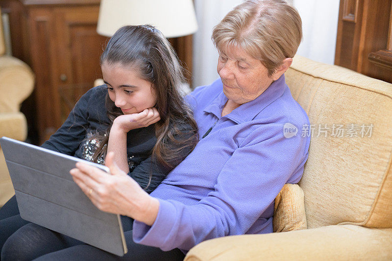 活跃的老年人。爷爷奶奶的爱。Covid - 19所示。一位老太太和她的孙女在客厅玩平板电脑